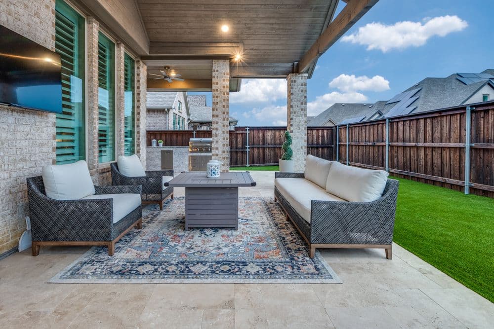 Modern outdoor patio with comfortable seating, stylish rug, and landscaped yard.